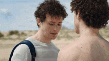 two men with curly hair are looking at each other in the desert