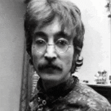 a man with glasses and a mustache is looking at the camera in a black and white photo .
