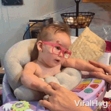 a baby wearing pink glasses is sitting in a high chair being held by a woman ..
