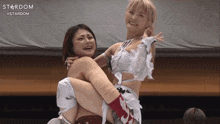 a female wrestler is carrying another wrestler in her arms with the word stardom on the bottom right
