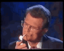 a man in a suit and tie is smoking a cigarette while wearing glasses .