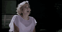 a woman in a pink dress and pearls is dancing in a dark room .