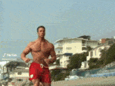 a shirtless man in red swim trunks runs on a beach