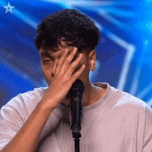 a man covering his face in front of a microphone with a blue star in the background