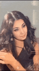 a woman with long dark hair is wearing a black dress and earrings .