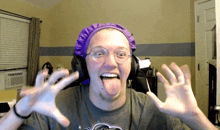 a man wearing headphones and a purple hat is sticking out his tongue