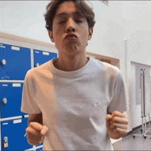 a man in a white t-shirt is making a funny face in front of blue lockers
