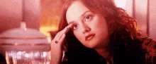 a woman is sitting at a table with her hand on her forehead and looking up .