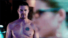 a shirtless man with a tattoo on his chest is looking at another man .