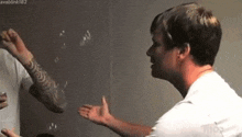 two men are playing with soap bubbles in front of a wall .