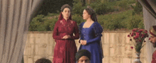 two women in dresses are standing next to each other in front of a wall .