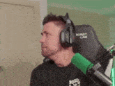 a man wearing headphones and a black shirt is sitting in front of a green microphone ..