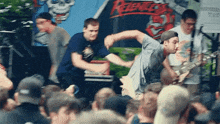 a man playing a guitar in front of a crowd with a rebellion sign in the background