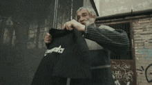 a man with a beard is holding up a black t-shirt with graffiti on it that says ' graffiti '