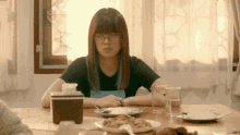 a woman wearing glasses sits at a table with a plate of food