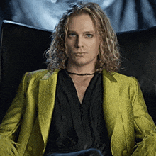 a man with long blonde hair wearing a black shirt and a yellow jacket