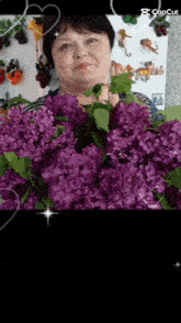 a woman is holding purple flowers in front of a refrigerator