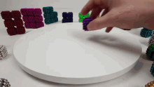 a person 's hand is reaching for a purple ball on a white surface