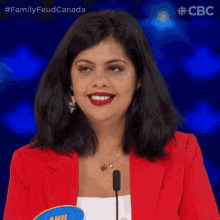 a woman in a red jacket stands in front of a microphone with the words family feud canada on the bottom