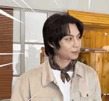 a man wearing a scarf around his neck and a jacket is standing in front of a window .