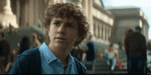 a young man with curly hair is standing in front of a crowd of people