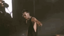 a man wearing sunglasses and a black tank top is standing on a stage in a dark room .