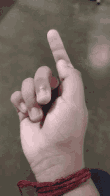 a person 's hand with a red string around their wrist is pointing up