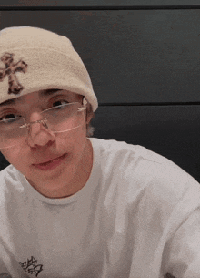 a young man wearing glasses and a beanie has a cross on his hat