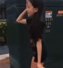 a young girl talking on a cell phone in front of a green box that says 10324 on it