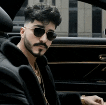 a man wearing sunglasses and a fur coat sitting in a car