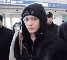 a man wearing a hooded jacket and a beanie is walking through an airport