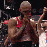 a basketball player wipes his face with a red towel in front of a beko sign