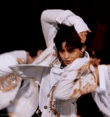 a man in a white jacket is dancing on a stage while wearing a microphone .