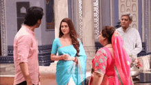 a group of people are standing around a woman in a blue saree .