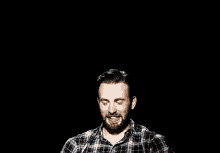 a man with a beard is covering his ear with his hand in a black background .