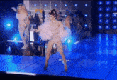 a group of drag queens are dancing on a stage with blue lights behind them