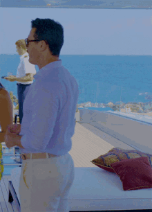a man in a blue shirt and tan pants stands on a deck overlooking the ocean