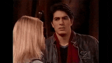 a man and a woman are looking at each other . the man is wearing a leather jacket and a red scarf .