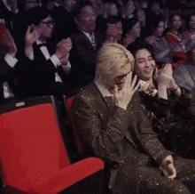 a man in a suit sits next to a woman in a black dress who is clapping