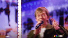 a man singing into a microphone with the nbc logo on the bottom right