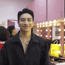 a man in a black shirt is smiling in front of a mirror with a yellow bag that says kk on it