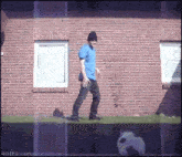 a man in a blue shirt and black hat is walking in front of a brick building