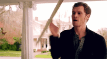 a man in a black suit is standing on a porch holding a pole .