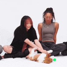 two women are sitting on the floor petting a brown and white dog