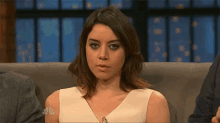 a woman in a white dress is sitting on a couch making a face .