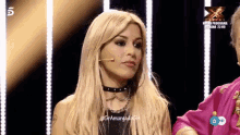 a woman in a choker stands in front of a microphone on a television screen that says ' x factor ' on it