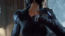 a woman in a black suit is holding a gun in her hand