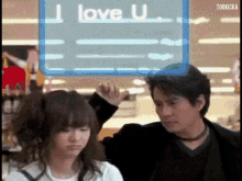 a man and a woman are standing in front of a sign that says i love u