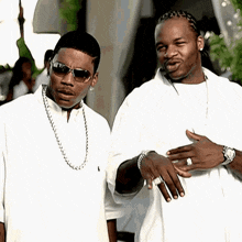 a man wearing sunglasses stands next to another man wearing white shirts