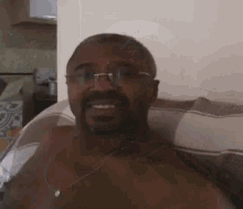 a shirtless man with glasses is sitting on a couch .